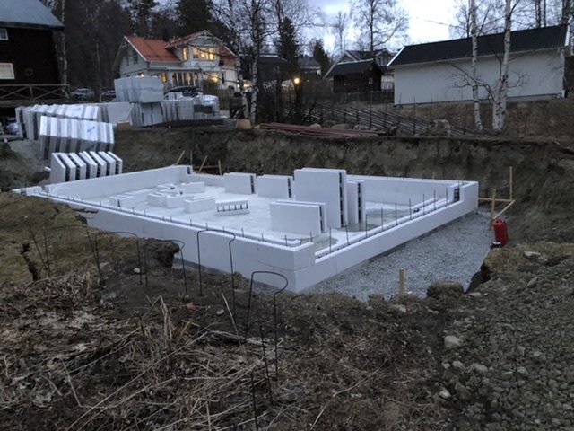 Grundläggning med termoblock på en byggplats med omgivande grävmaskin och byggmaterial i bakgrunden.