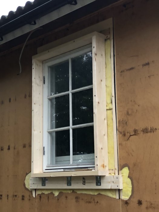 Ny träram för fönsterinstallation med regel, vinkeljärn och gammalt fönster innanför på vägg.