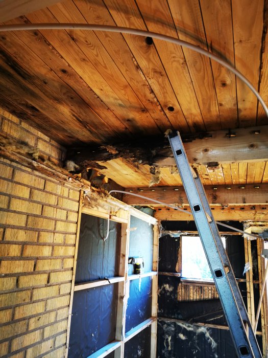 Skadad bjälke i garage med synlig röta och borttagen isolering samt väggmaterial.