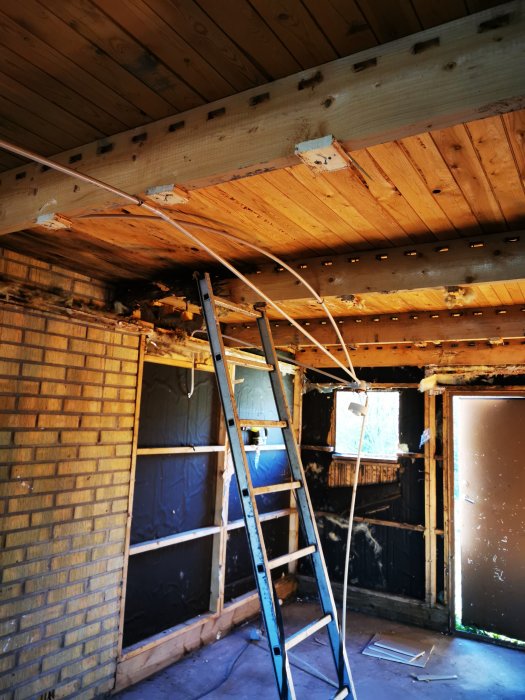 Rivet garageinteriör med synliga träbjälkar och skador, stege på plats och delvis nedmonterade väggar.