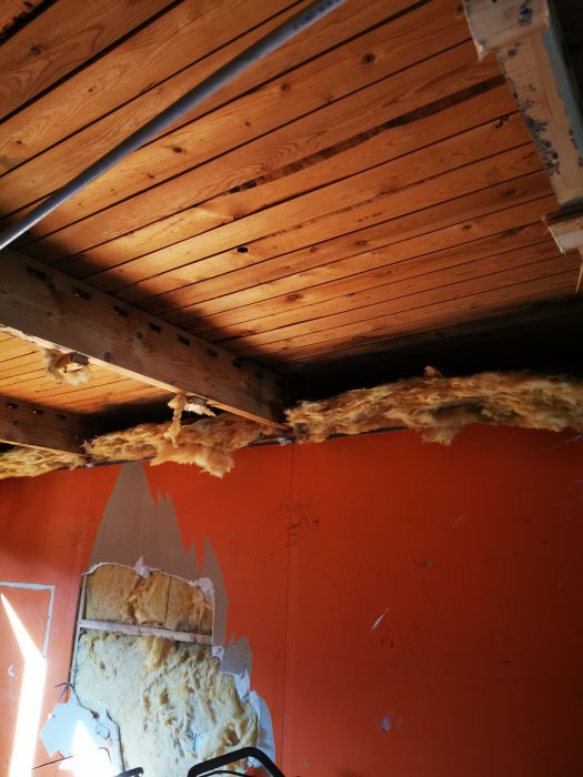 Rutten bjälke och skadad isolering i takskelettet i ett garage med synliga vattenskador.
