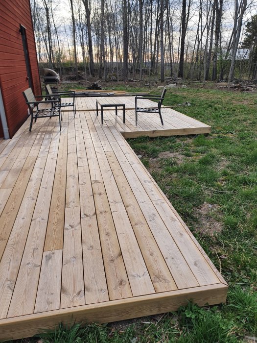 Trädäck i trädgården med uteplatsmöbler nära skogskant efter vintern.