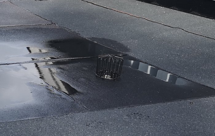 Vattenansamling på garagetak med ny lagd papp, dålig lutning mot en synlig brunn.