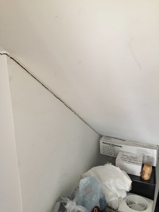 Sprækken mellem væg og loft i en trappeopgang, med diverse genstande og en kasse med "National Panasonic" i hjørnet.