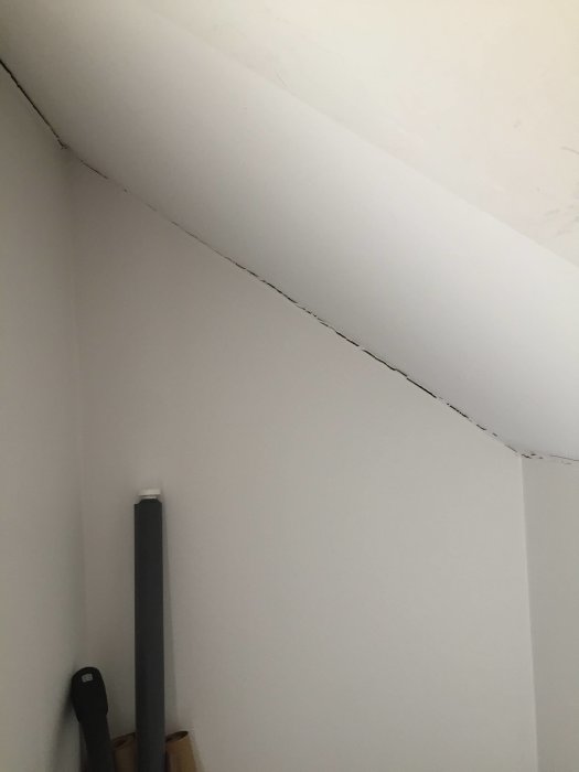 Sprække mellem loft og væg i et trappeområde, hvor strukturen viser bevægelse; sort rør op ad væggen.