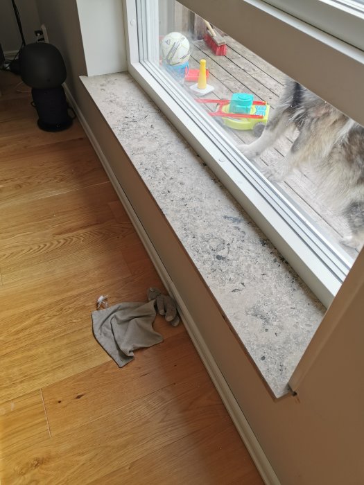 Nyinstallerad kalkstensfönsterbänk i Jura Grey i rum med trähögkant och leksaker samt hund utanför fönstret.