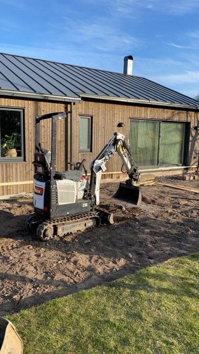 Minigrävare framför hus med upplöst mark vid fibergrävningsarbete.