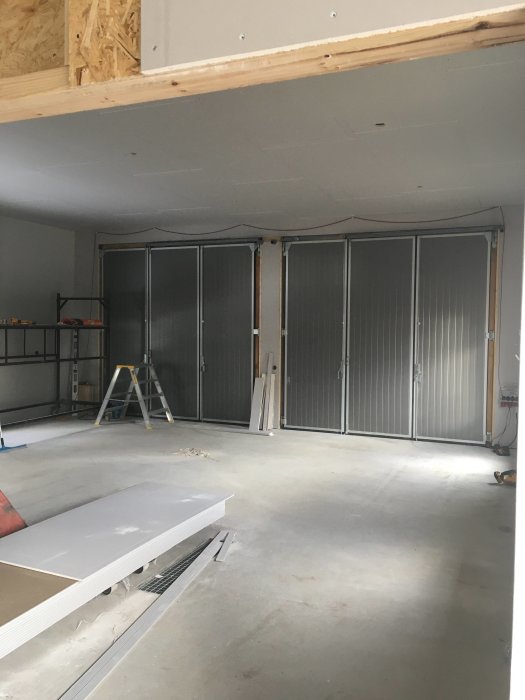Nyinstallerad OSB och gipstak i en garageinteriör med höga metalldörrar och byggmaterial på golvet.