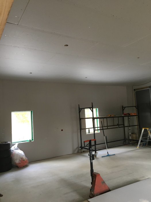 Ett inomhus byggprojekt visar nyinstallerade gipsskivor på taket i ett rum med ställningar och byggmaterial.