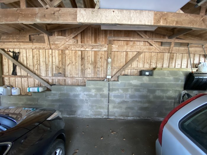 En dubbelcarport med trätakstolar, betongväggar och två parkerade bilar.