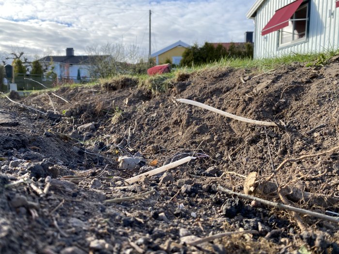 Ytligt liggande fiberkabel i avgrävd jord nära en sluttning på en tomt.