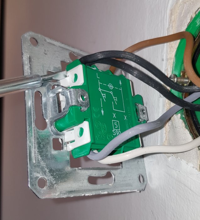 Öppen elektrisk strömbrytardosa med fem kablar anslutna: svarta, bruna, vita, gråa och blåa, monterad på en vägg.