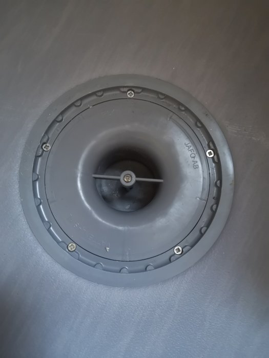 Installationsvy av en grå röranslutning för avlopp i ett pågående badrumsprojekt, med skruvar runt kanten.