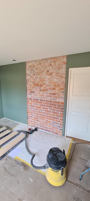 Sovrum under renovering med en exponerad röd tegelmurstock vid en vägghörna, bredvid en vit dörr och grönmålade väggar.