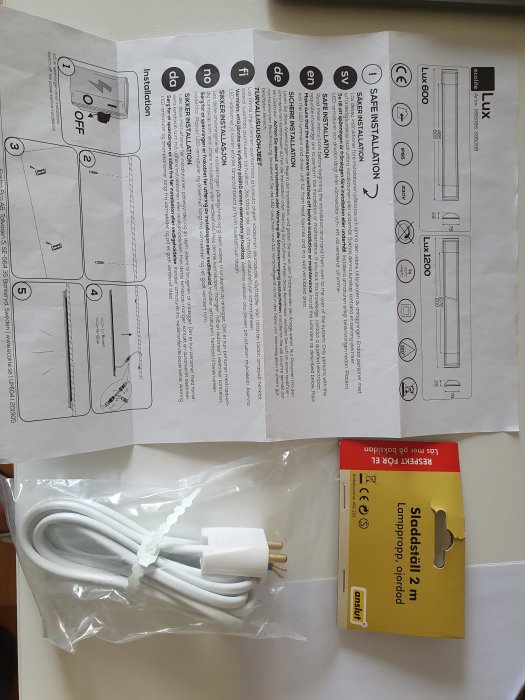 Instruktionsblad för LED-armatur med diagram och text samt en oöppnad lamppropp i förpackning.