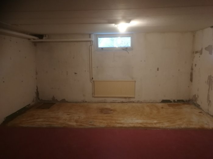 Källarrum med bortriven panel, synliga isoleringsrester och putsade väggar med hål och fläckar.