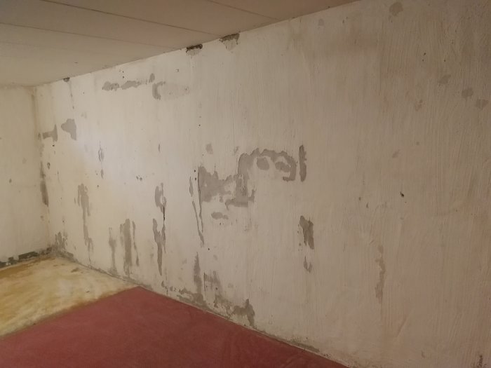 Renoveringsprojekt av källare med vägg där puts har petats ner, visar skador och ojämnheter.