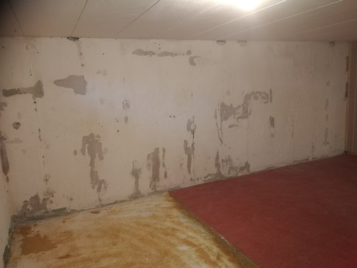 Källarrum med ojämna väggar där träpanel och isolering har tagits bort, med synliga hål och putsavfall.