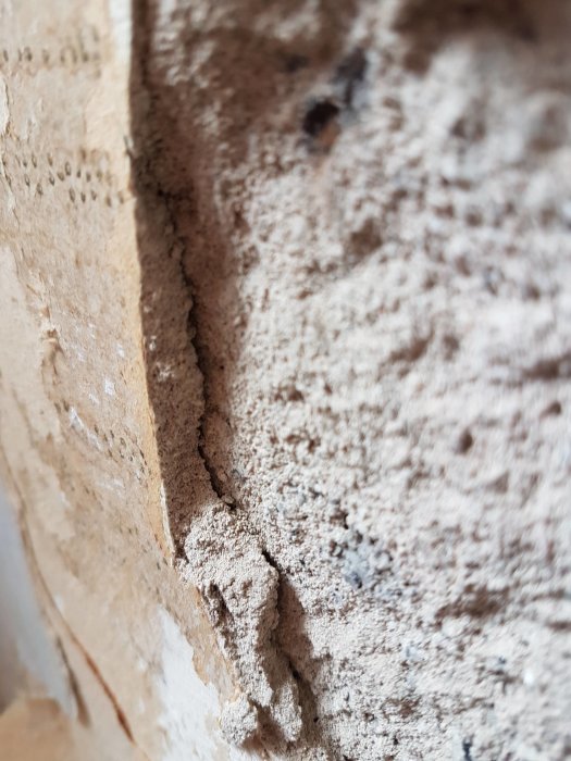 Närbild på en vägg med lösa lager av spruckna tapeter och puts som hänger fritt från underliggande betong.
