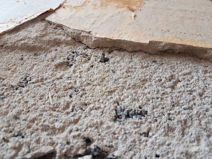 Närbild på en vägg med lösa puts- och tapetlager där den underliggande betongen är synlig.