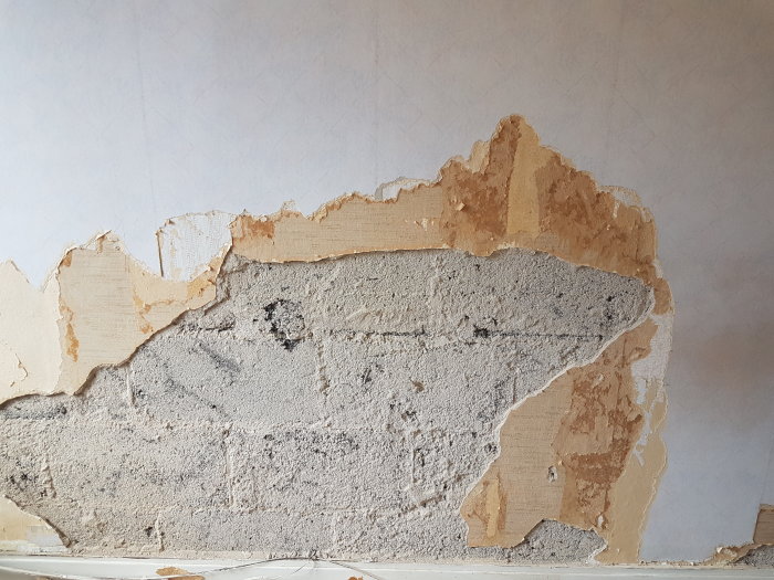 Vägg med delvis bortskrapad tapet som avslöjar underliggande betong och puts.