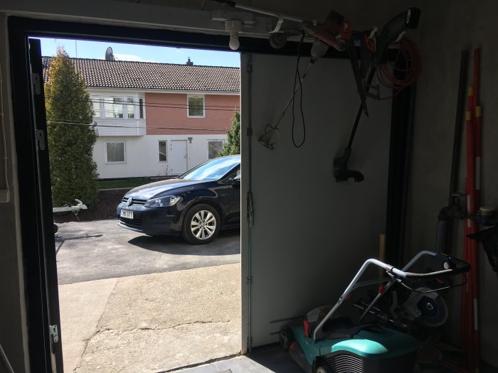 Öppen garageport med synlig slitage på kanterna, synlig bil utanför och verktyg i garaget.