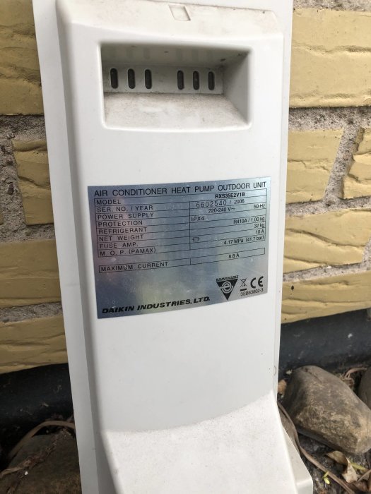Utomhusenhet för luftvärmepump av märket Daikin, monterad nära en husvägg, med teknisk information synlig på etiketten.