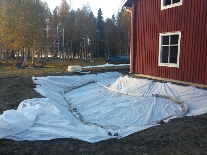 Markduk med dräneringsledning utlagd vid husgavel för förberedelse av uteplats med järnsand och natursingel.