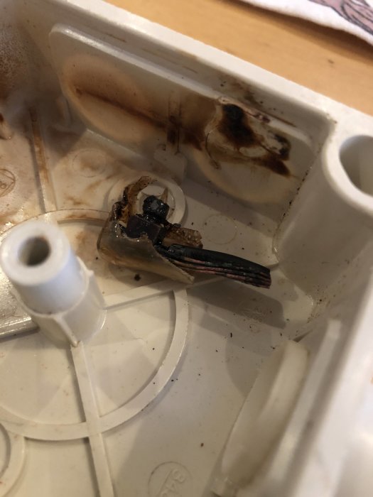 Smält skruvklämma i en elcentral med tecken på varmgång och brandskador, indikerar elektriskt fel.