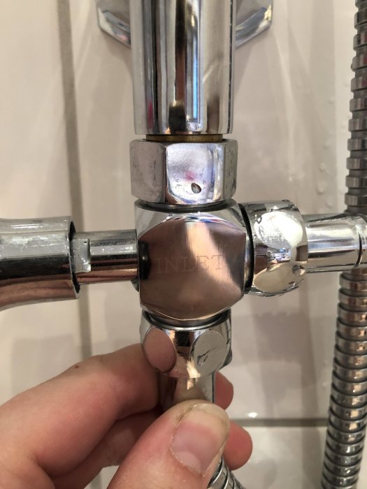 Närbild på en kromad T-koppling med glipa som läcker vatten, del av nyinstallerad dusch.