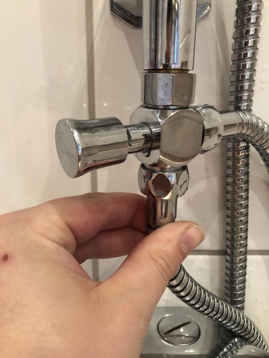 Hand som pekar på en glipa vid en T-koppling på en kromad duschblandare, där läckage uppstår.
