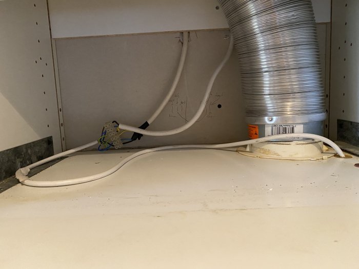 Äldre spisfläkt monterad under köksskåp med synliga elanslutningar och ventilationsslang.