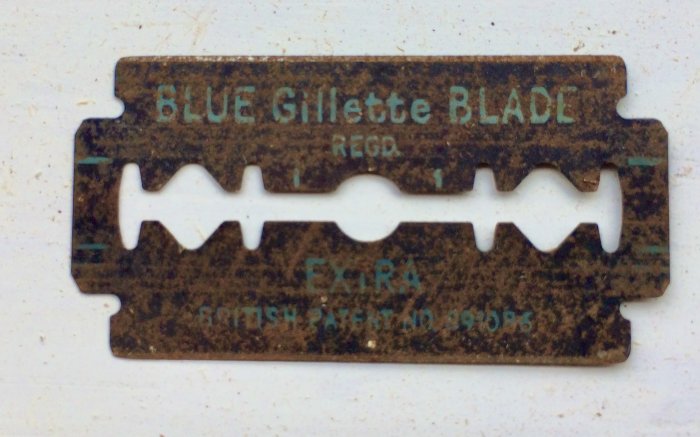 Gamla rostiga rakbladet "Blue Gillette Blade" på en vit yta.