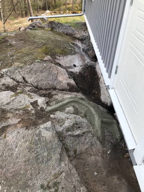 Vattenansamling i en klippskreva nära husets grund på en fastighet med synligt berg i terrängen.