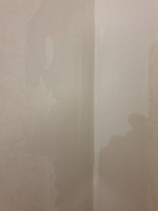 Vägg med spackelremsor som lossnar, synliga skarvar och avskalad papp i hörnet.
