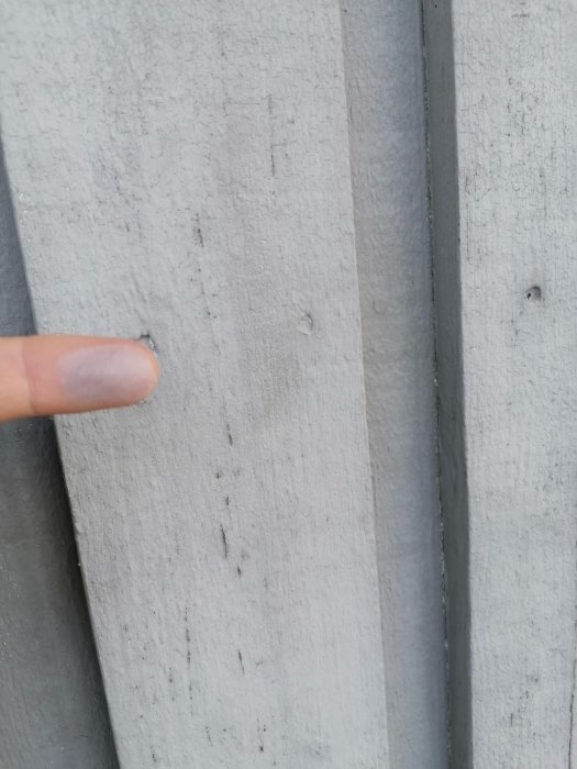 Mjölkig utfällning på en husfasabd målad med akrylatfärg, finger pekar på avvikelsen.