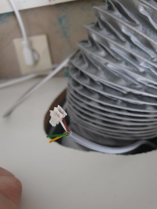 Flexibel ventilationsslang och flerkärnig kabel med snabbkontakt mot en vägg.