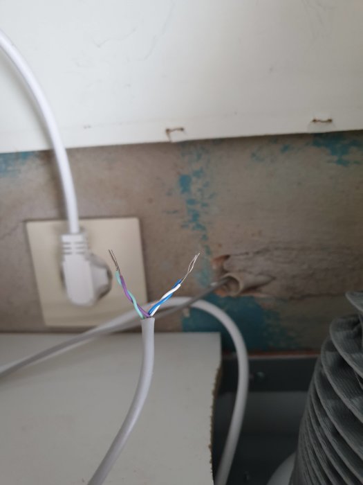 Elektriska kablar med exponerade ändar i en vit mantel, inkluderar blå, vit, turkos och lila trådar.