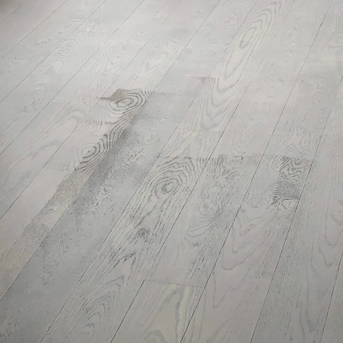 Nyslipat trägolv med ojämn betsfärg och lack, mörkare partier längs med träådring.