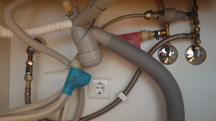 Rörkopplingar och slangar under diskbänk med röd och blå markering för Siemens diskmaskins vattenanslutningar.