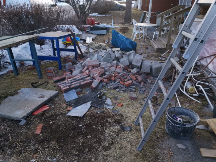 Nedmonterade tegelstenar och avfall efter skorstensrivning på en gräsmatta med stege och barns leksaker i bakgrunden.