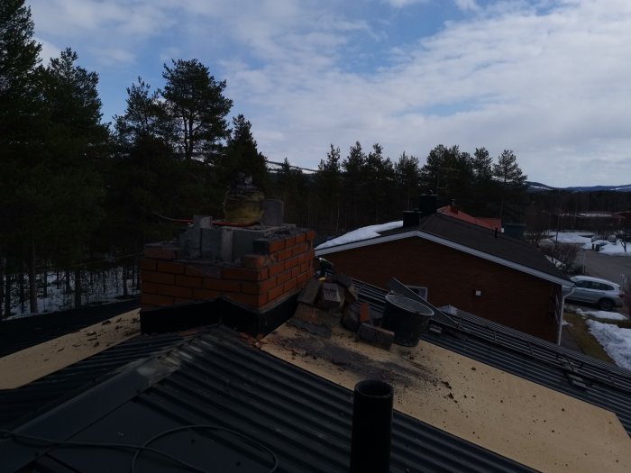 Skadad skorsten med synligt tegel och rester av plåt på ett hus under renovering på ett hustak.