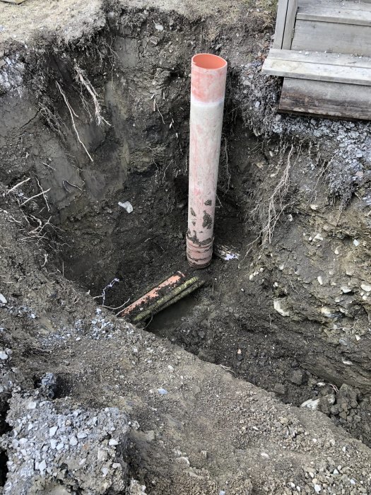 Uppgrävd plats för avlopp, el, vatten och bredband med synlig rörledning och kabel vid ett hus.