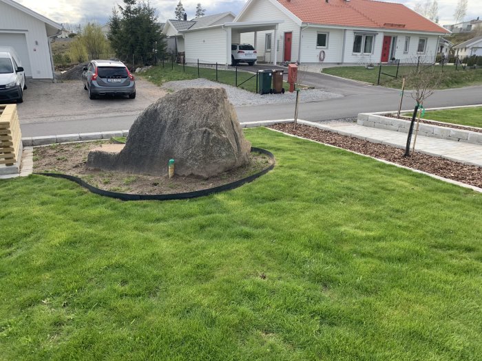 Stor sten i trädgård med gräsmatta runtom, väntar på plantering och dekoration.