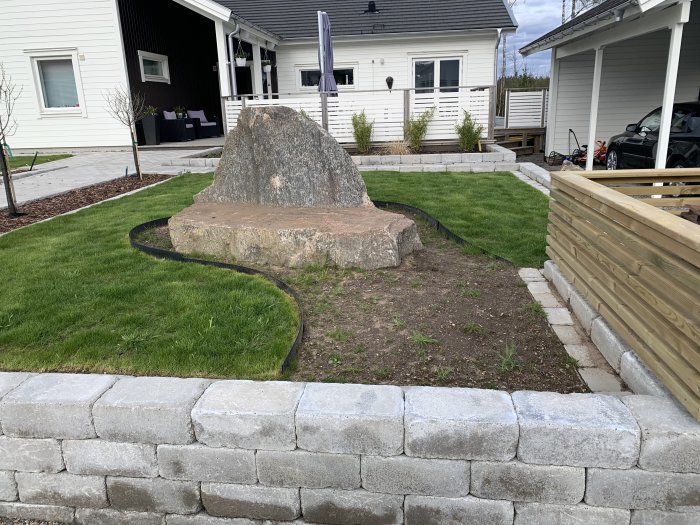 Stor sten i trädgård med omgivande nyplanterat gräs och jordklumpar som förbereds för plantering.