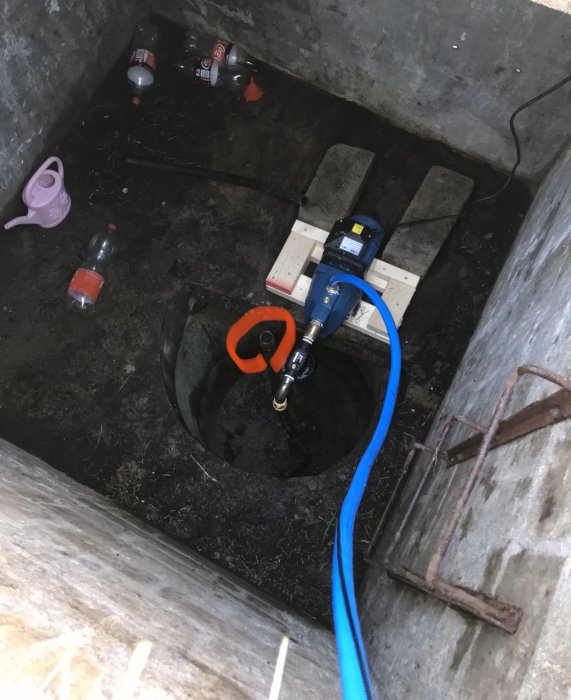 En brunn under mark med nytt pumpsystem och slangar, gammalt spett och tomma flaskor.