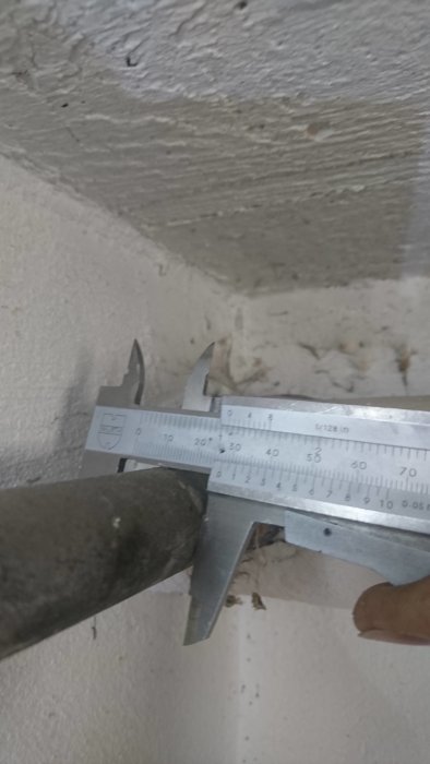 Mätning av ett gammalt galvat rör med en skjutmått för att bestämma ytterdiameter inför bytet till kopparrör.