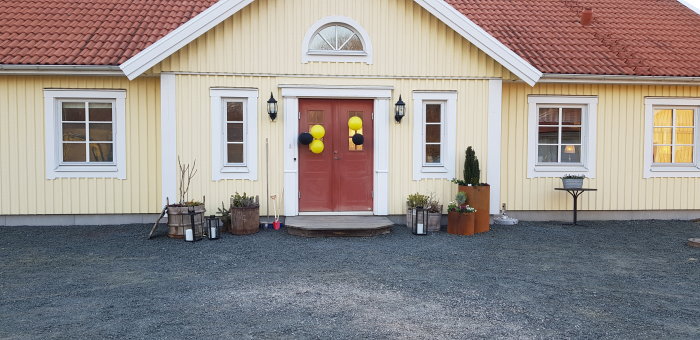 Amerikansk veranda med röd dörr och gula ballonger, ommålat hus i gult, träveranda och dekorativa krukor framför.