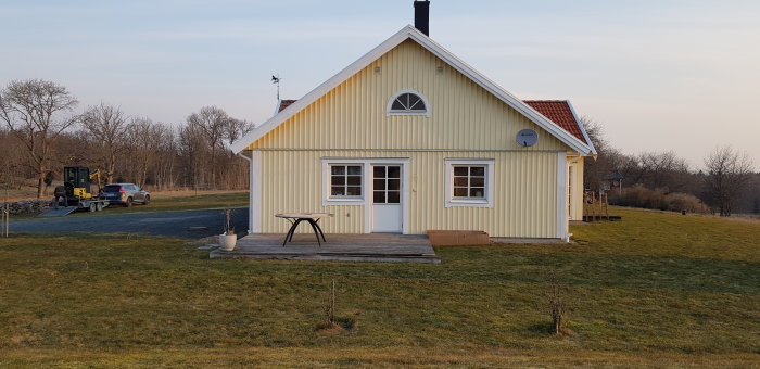 Gult hus med ny amerikansk veranda och röd shingel under klar himmel.