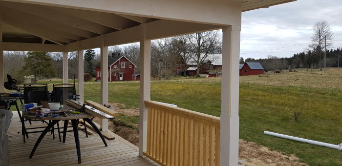 Halvfärdig veranda med byggmaterial och utsikt över lantlig gård.